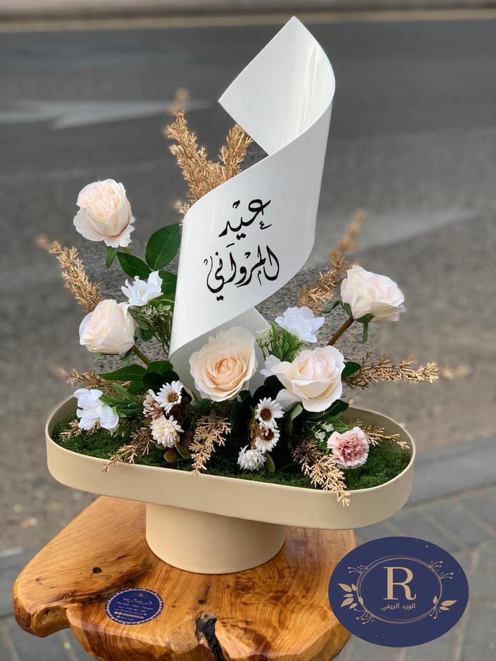 استاند عيد من الورد الكريمي مع لفافة كُتب عليها بالخط العربي