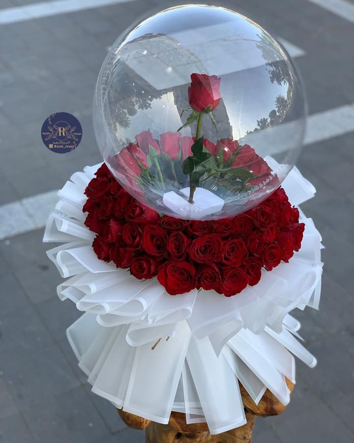 باقة ورد أحمر تعلوها وردة داخل كرة شفافة